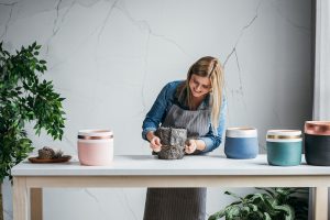 Pretty Caucasian blonde smiling woman artisan wrapping her handmade plant pot with a decorative paper.